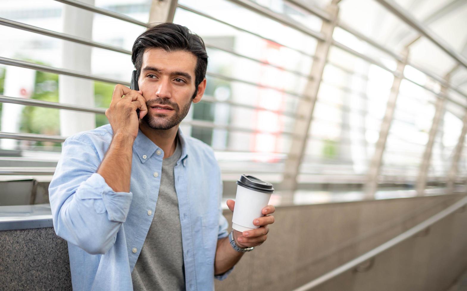 el hombre que sostiene una taza de café y usa un teléfono inteligente y habla con su amigo mientras espera a su amigo en el aeropuerto. foto