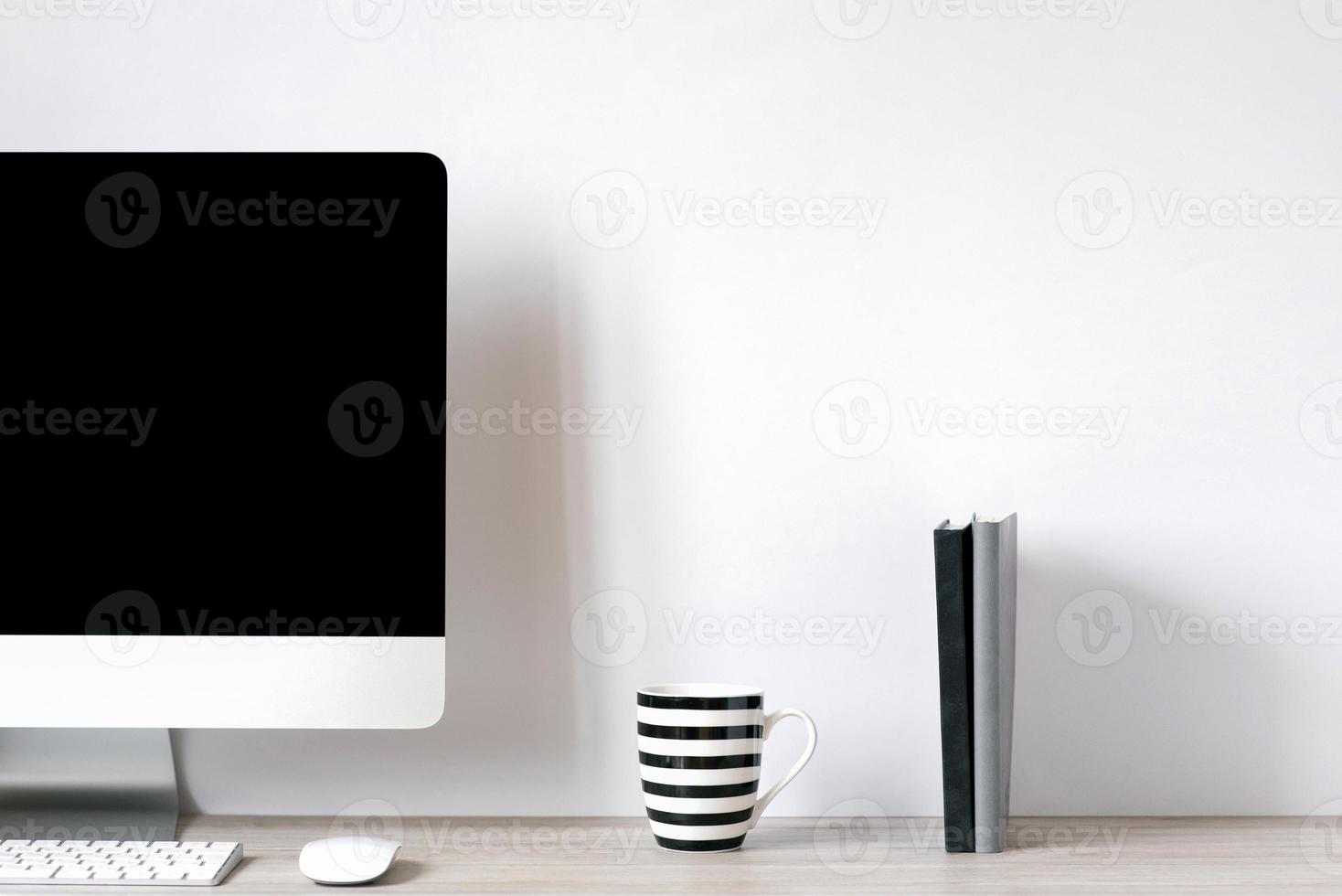 A laptop with a black blank screen, a mug with black and white stripes, notepads is on the desk of an office worker. Front view photo