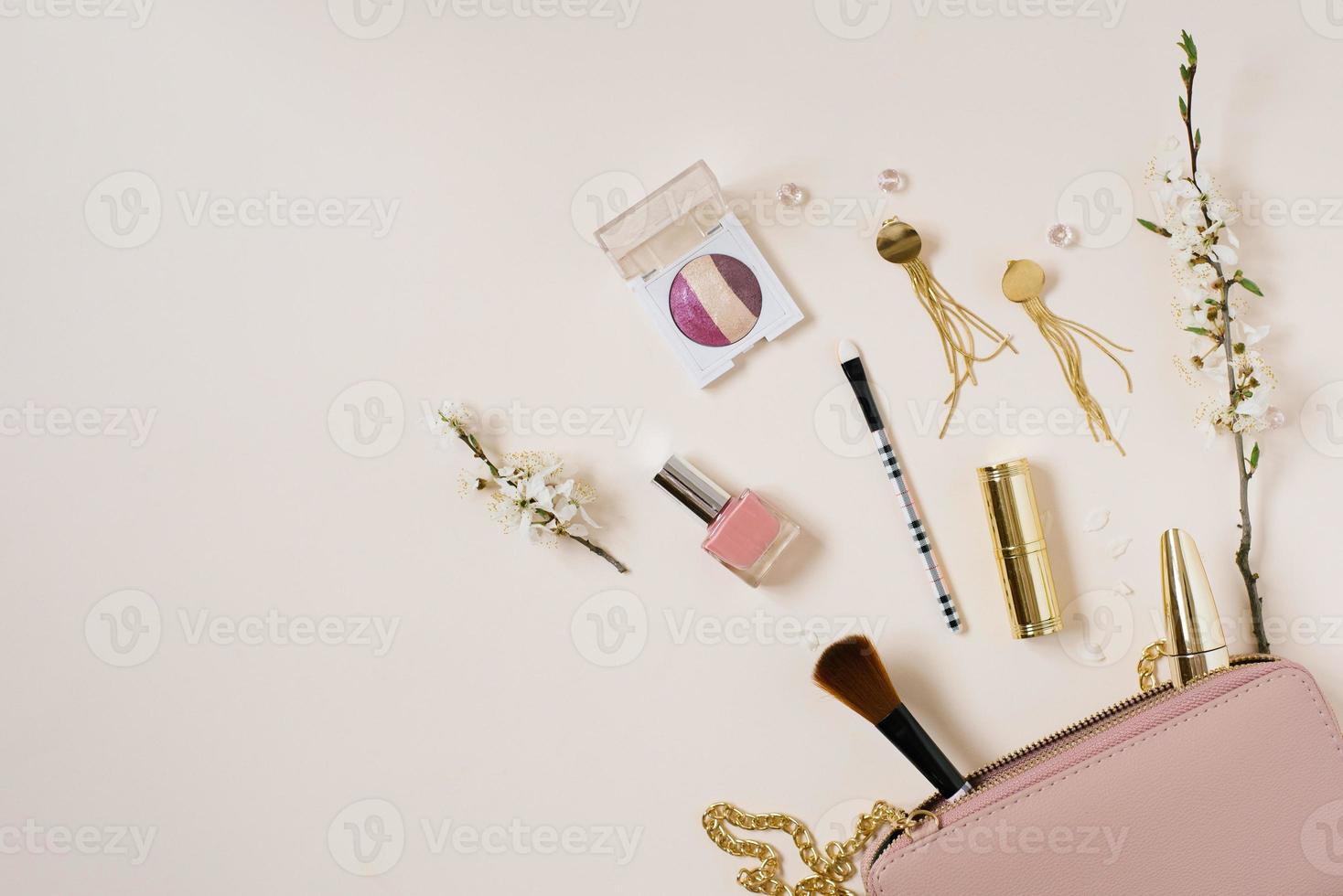 Women's desk with cosmetics, which lies next to a pink bag or cosmetic bag with copying space, apple tree flowers on a beige background. Top view. It was flat. The composition of the frame photo