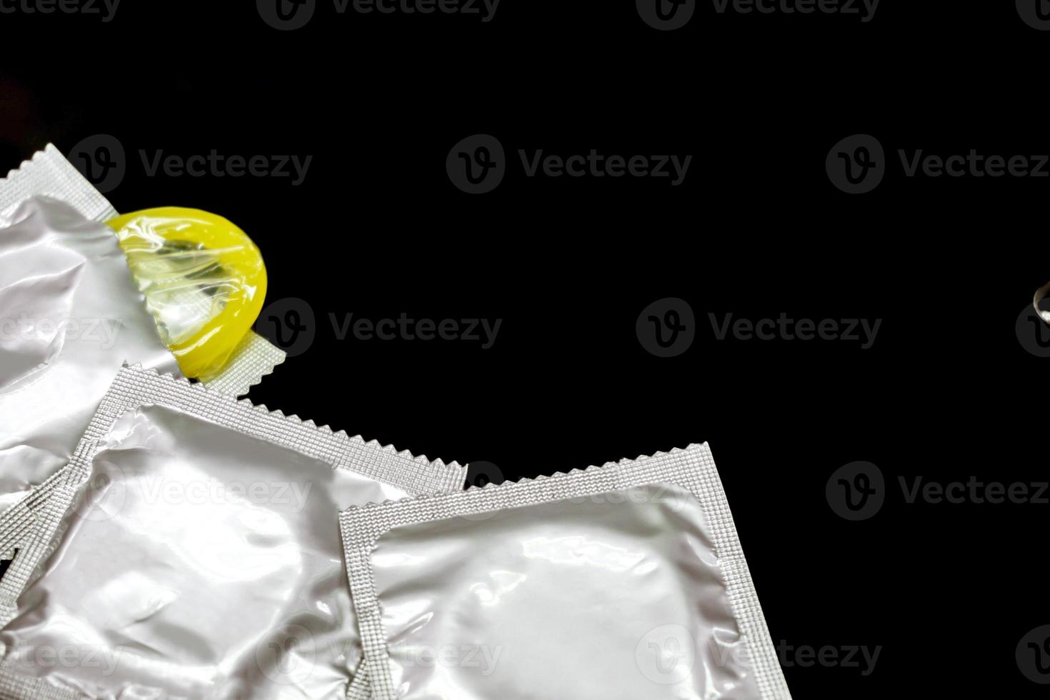 Condom in silver packages and one opened crops and do copy space isolate on  black background. photo