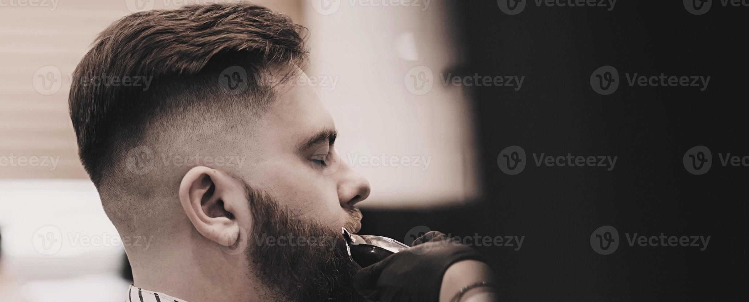 barber making haircut of bearded man photo