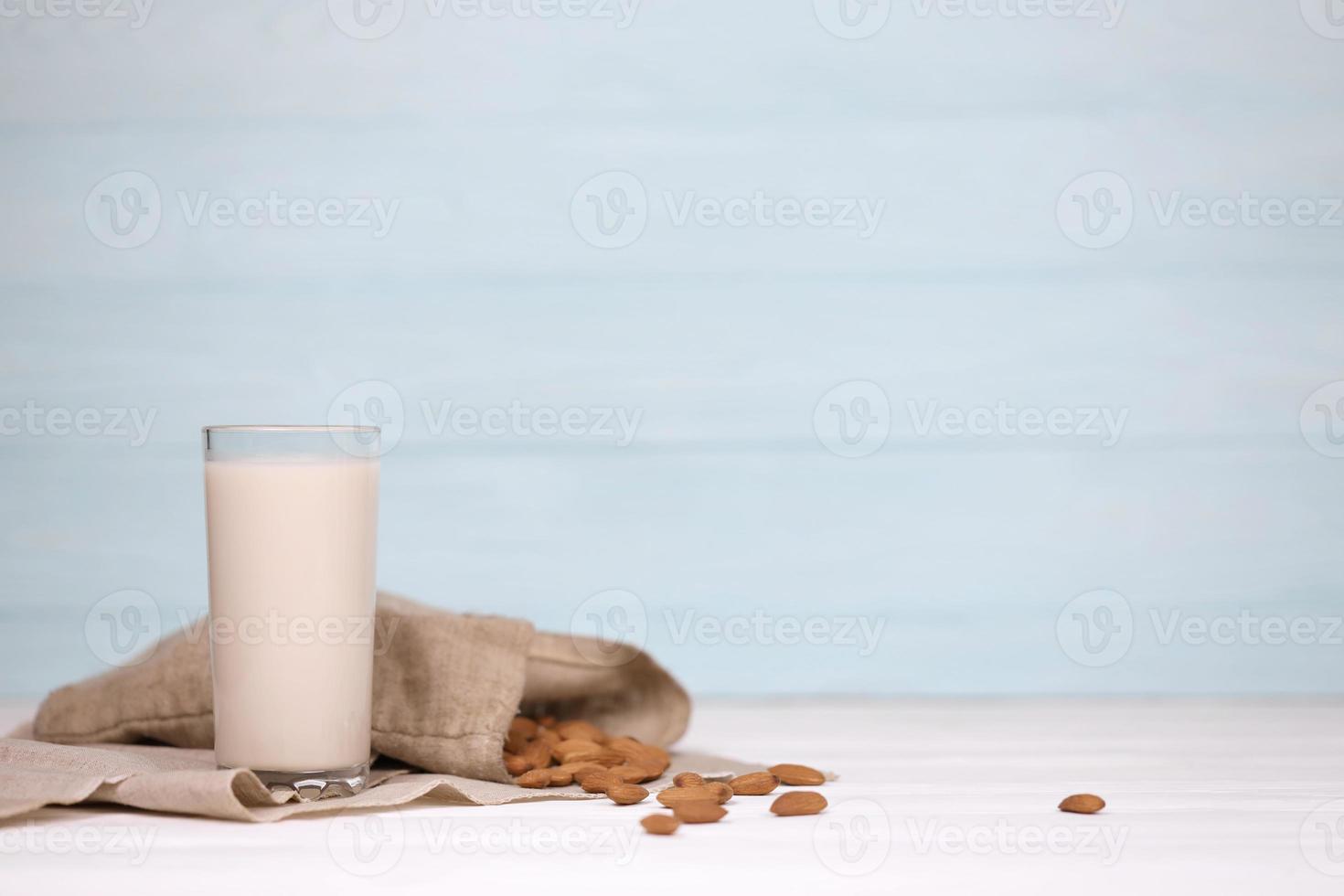 Glass of almond milk with almond nuts on canvas fabric on white wooden table. Dairy alternative milk for detox, healthy eating and diets photo