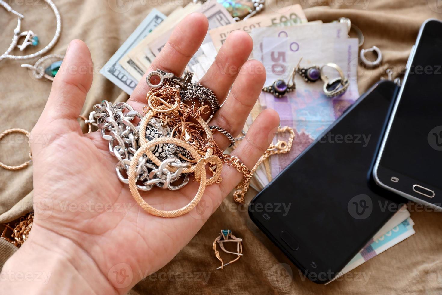 Marauders hand with bunch of stolen jewelry, money and smartphones on military uniform cloth fabric. Looting by Russian soldiers in the Ukrainian cities during Russian invasion on Ukraine photo