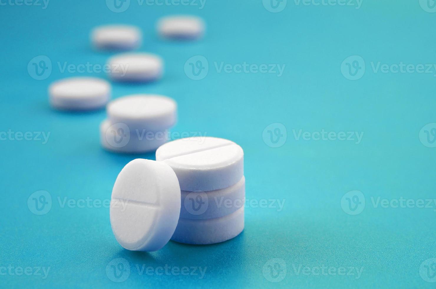 A few white tablets lie on a bright blue background surface. Background image on medical and pharmaceutical topics photo