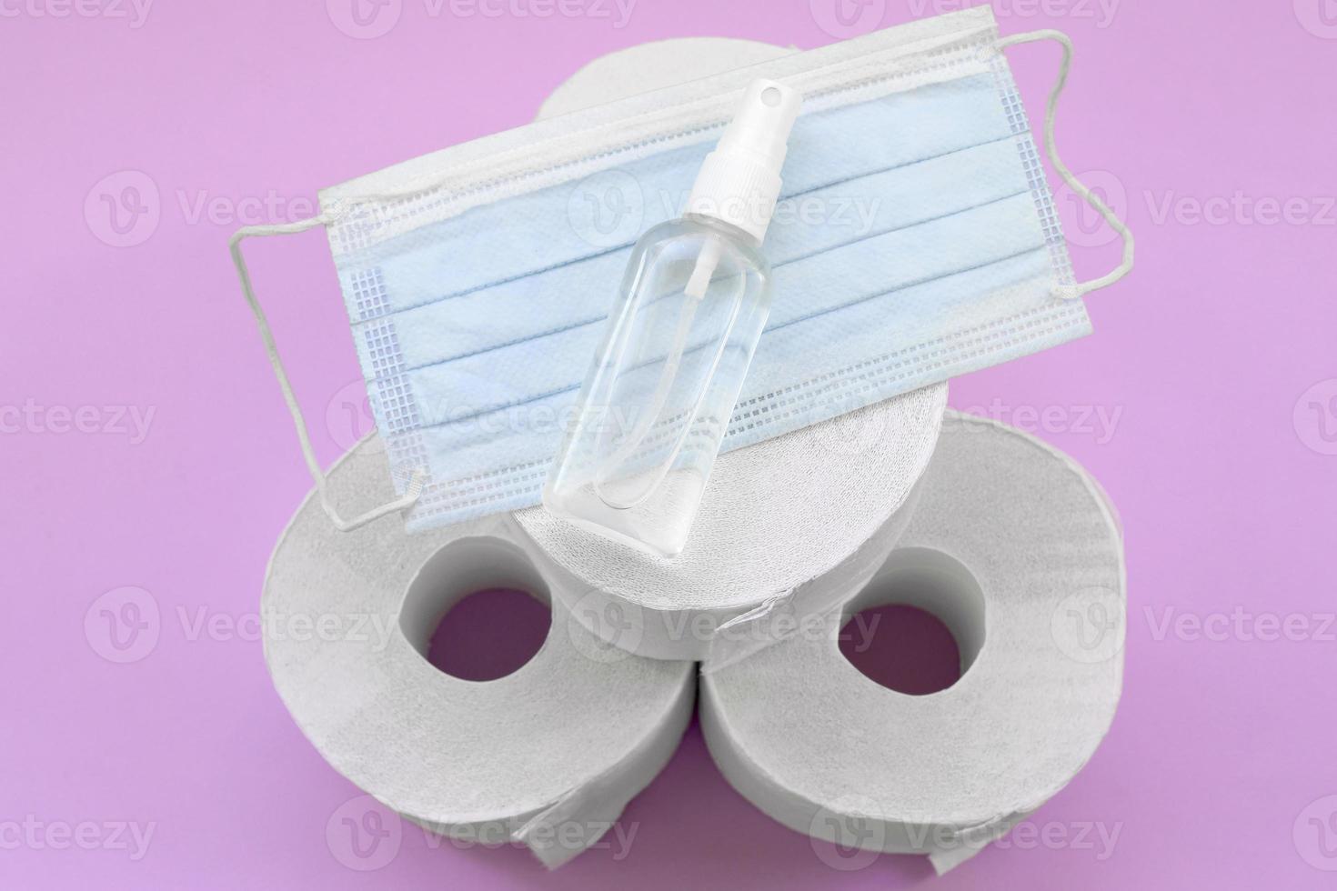 conjunto de artículos importantes para la cuarentena de covid-19. papel higiénico, mascarilla quirúrgica y desinfectante de manos sobre fondo lila. concepto de salud e higiene foto