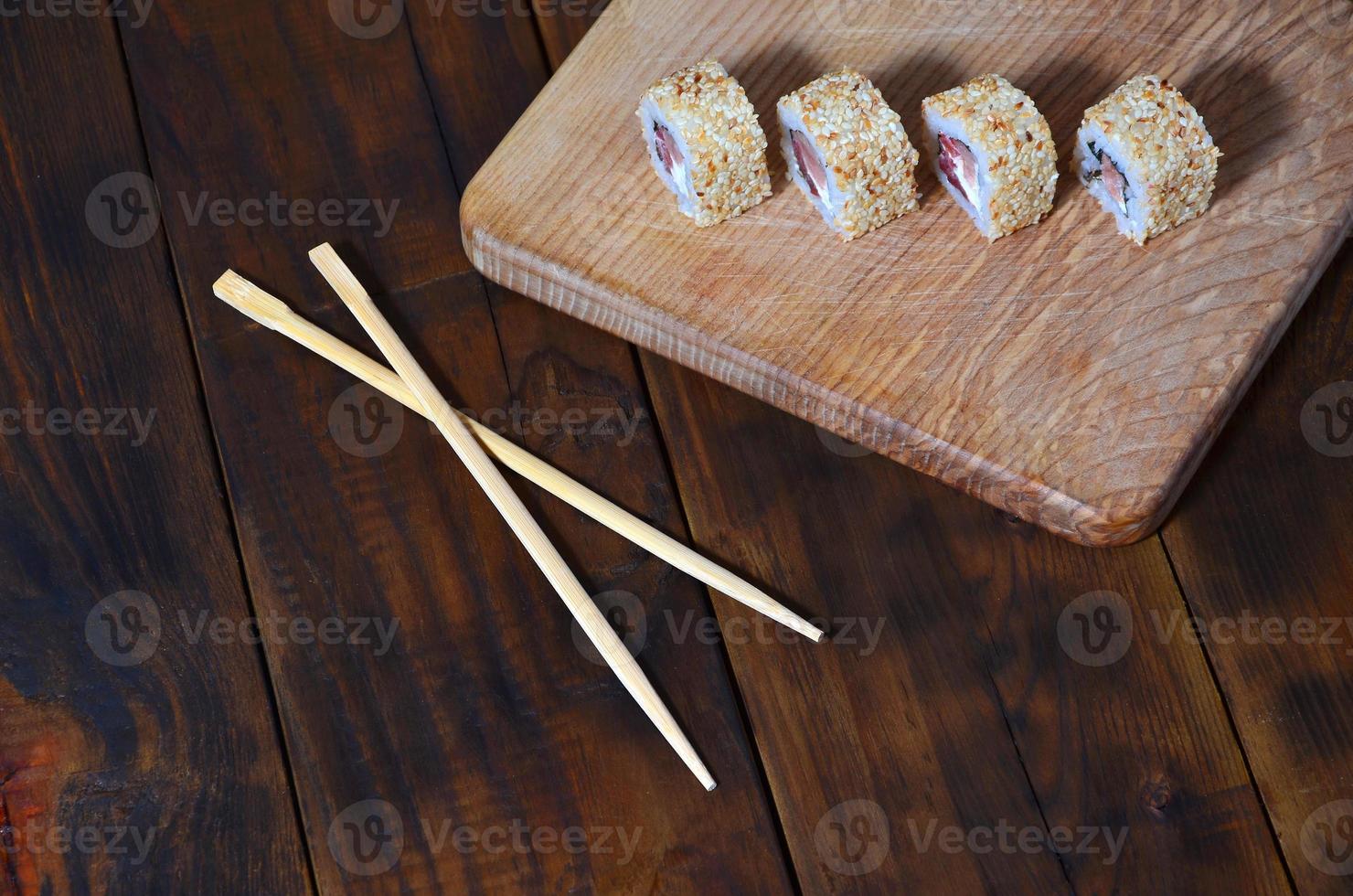 A detailed shot of a set of Japanese sushi rolls and a device for their use chopsticks, which are located on a wooden cutting board on a table in the kitchen of a sushi bar photo