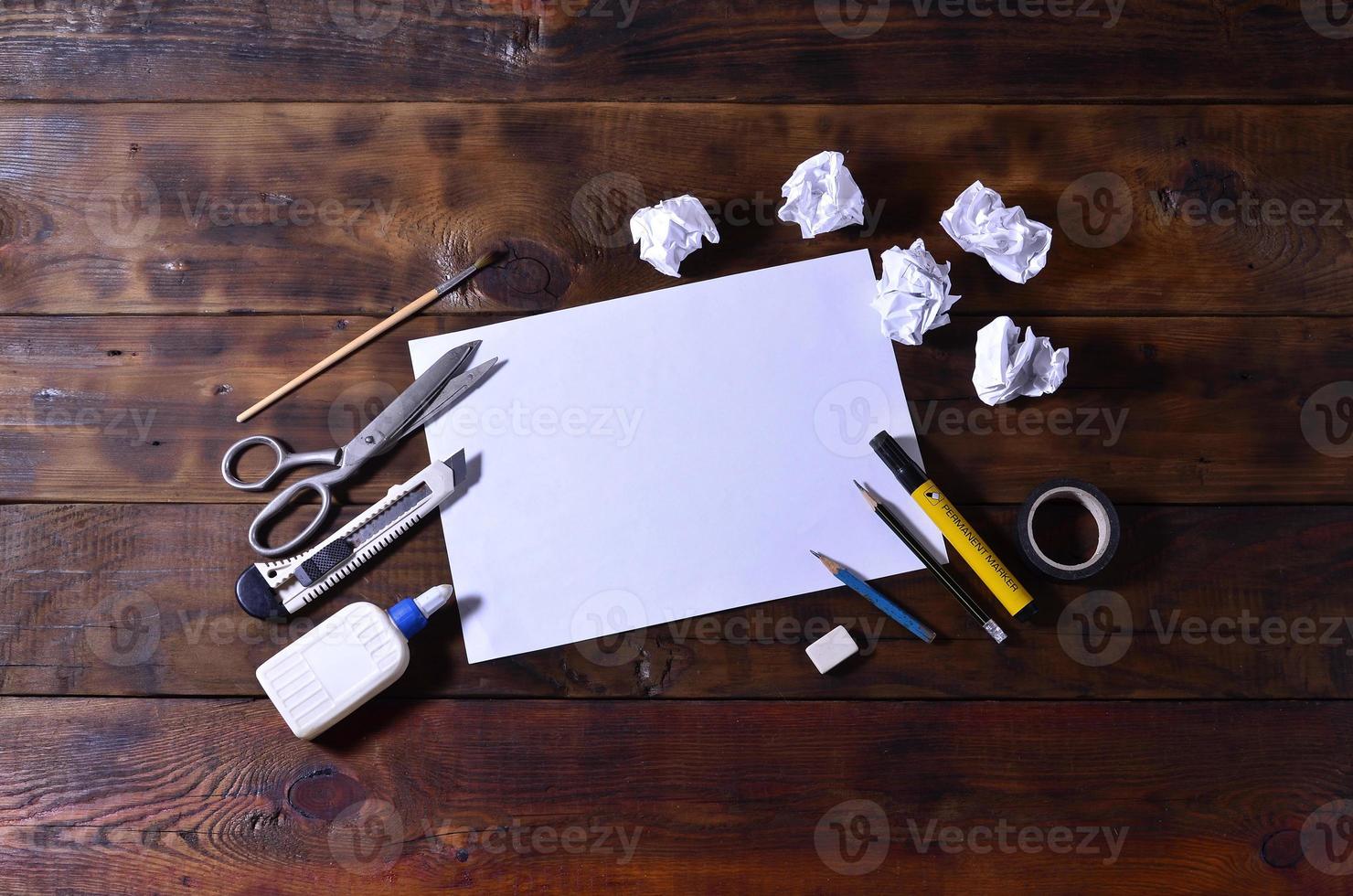 un bodegón de escuela u oficina con una hoja de papel en blanco y muchos suministros de oficina. los útiles escolares se encuentran sobre un fondo de madera marrón. lugar para texto foto