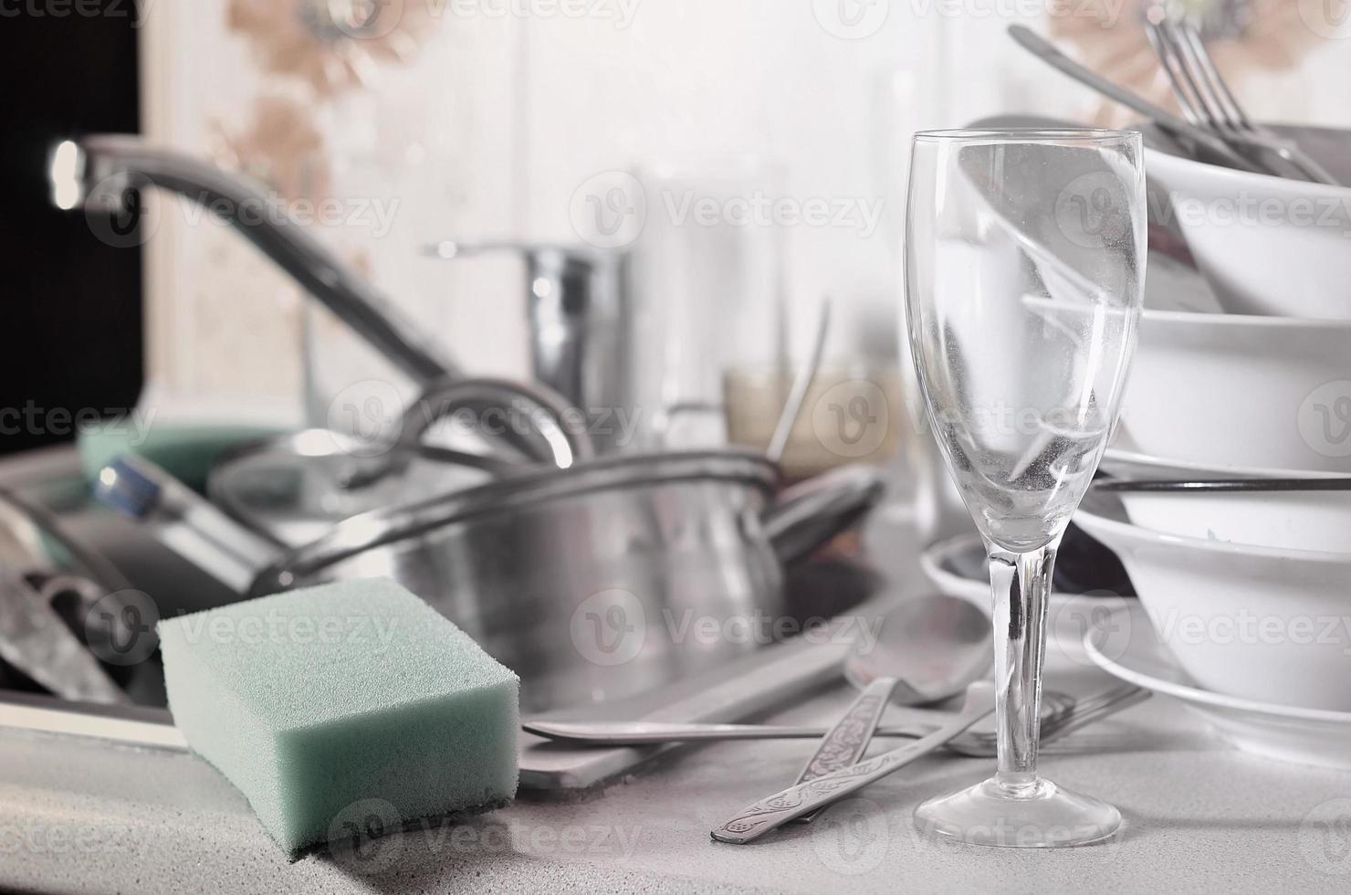 A huge pile of unwashed dishes in the kitchen sink and on the countertop photo