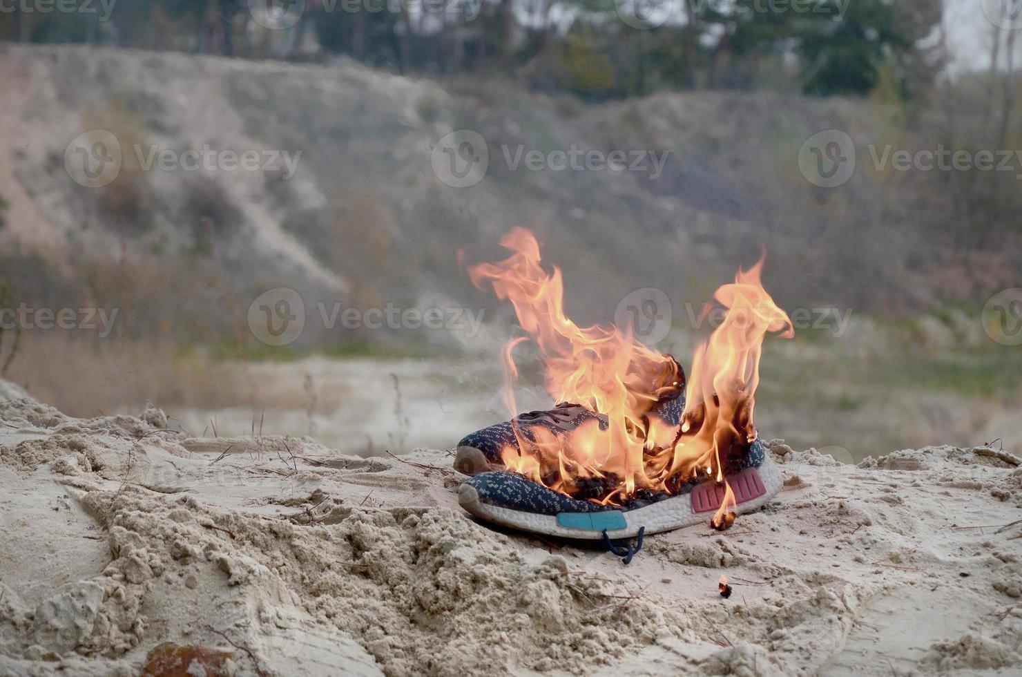 Burning sports sneakers or gym shoes on fire stand on sandy beach coast. Athlete burned out. Physical exertion during training concept photo