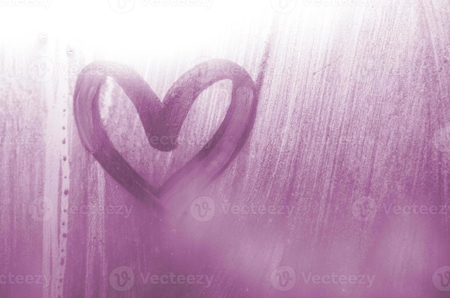 A heart-shaped drawing drawn by a finger on a misted glass in rainy weather photo