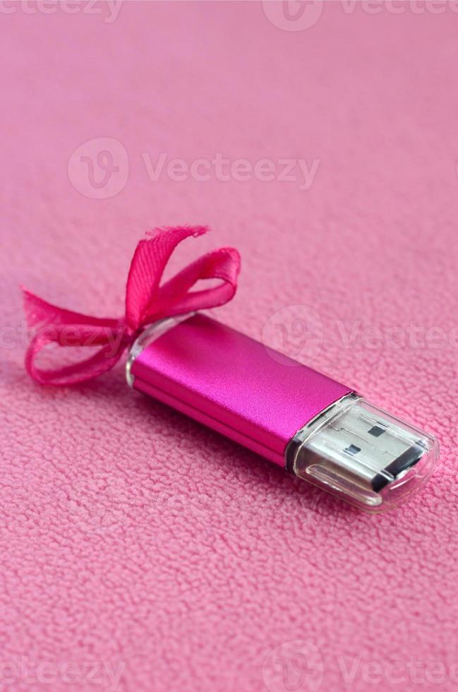 Brilliant pink usb flash memory card with a pink bow lies on a blanket of soft and furry light pink fleece fabric. Classic female gift design for a memory card photo