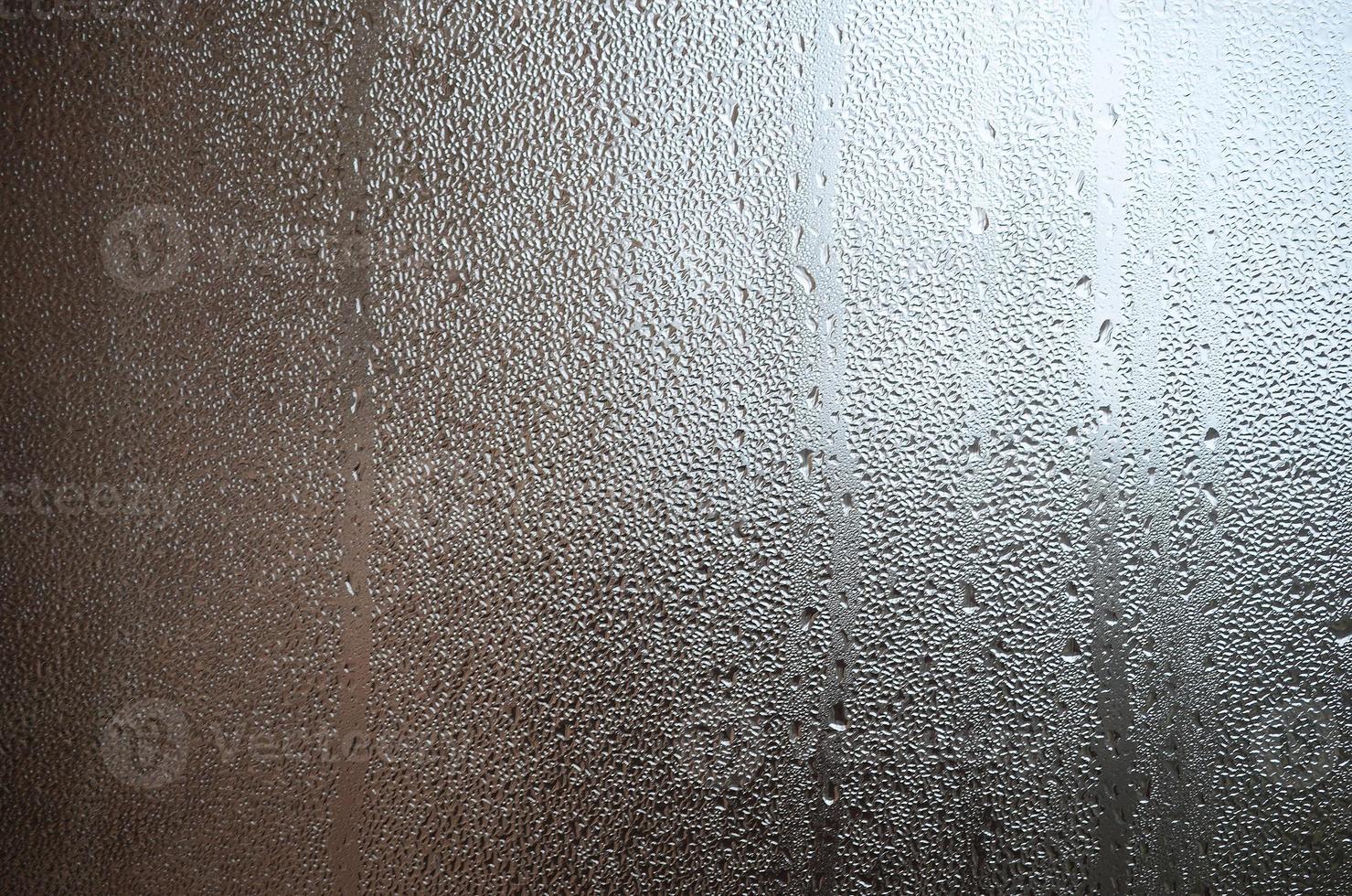 A photo of the glass surface of the window, covered with a multitude of droplets of various sizes. Background texture of a dense layer of condensate on glass