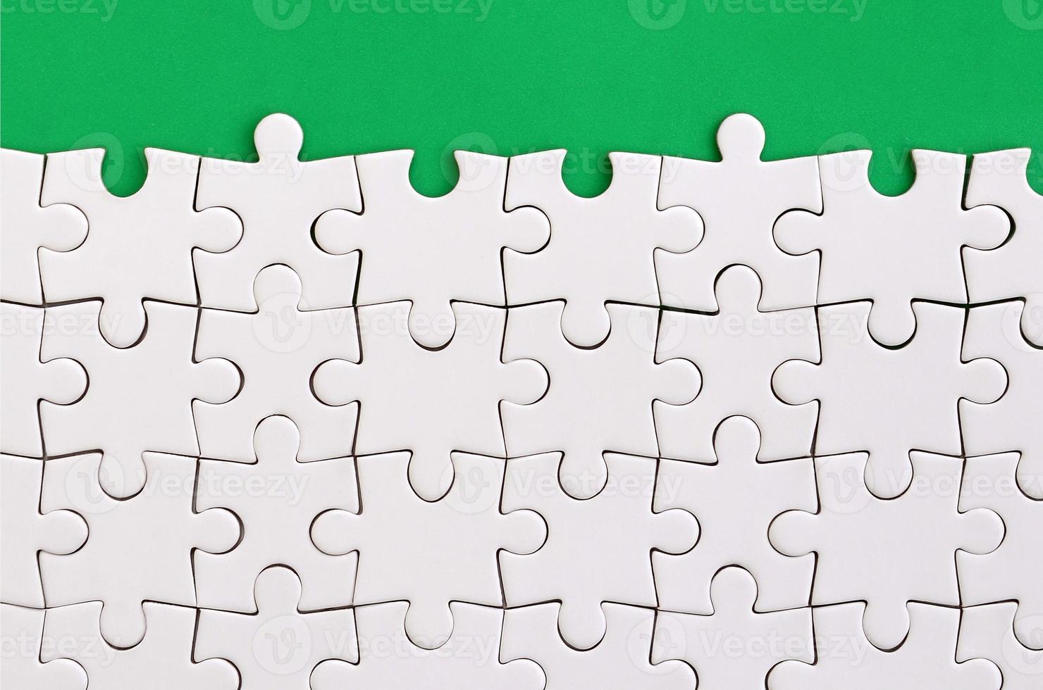 Fragment of a folded white jigsaw puzzle on the background of a green plastic surface. Texture photo with copy space for text