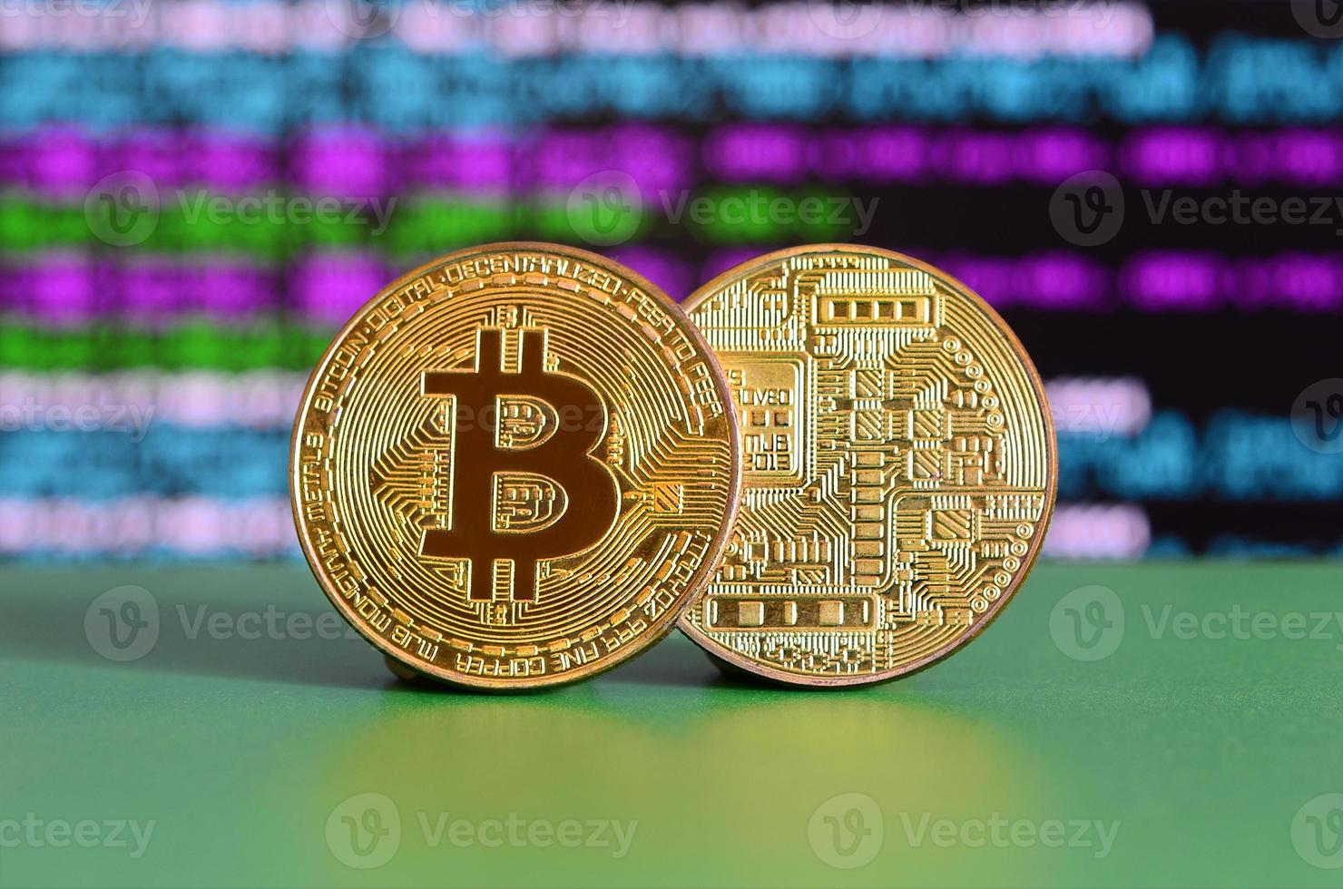 Two gold bitcoins lie on the green surface on the background of the display, which shows the process of mining the crypto currency photo