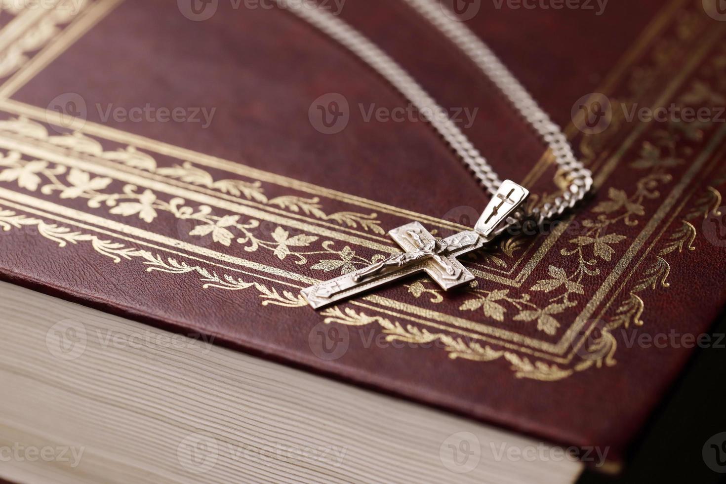 collar de plata con cruz crucifijo en el libro de la santa biblia cristiana sobre una mesa de madera negra. pidiendo bendiciones de dios con el poder de la santidad, que trae suerte foto