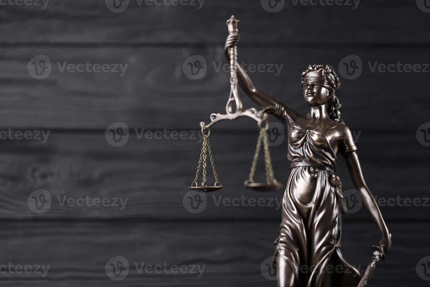 The Statue of Justice - lady justice or justitia the Roman goddess of Justice. Statue on black wooden wall. Concept of judicial trial, courtroom process and lawyers work photo