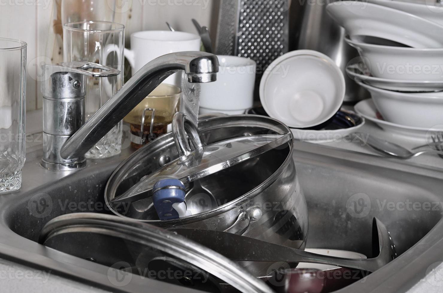 A huge pile of unwashed dishes in the kitchen sink and on the countertop photo