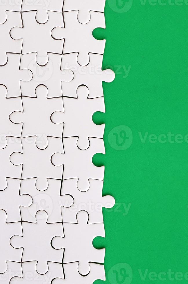 Fragment of a folded white jigsaw puzzle on the background of a green plastic surface. Texture photo with copy space for text