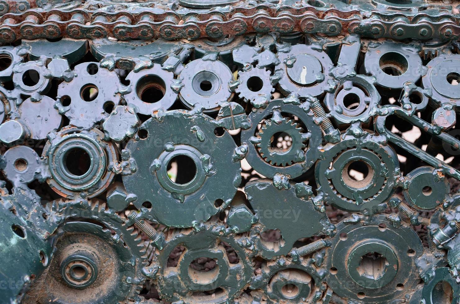 A composition of a set of gears and car parts that are welded to each other and painted green. Grunge steampunk texture photo