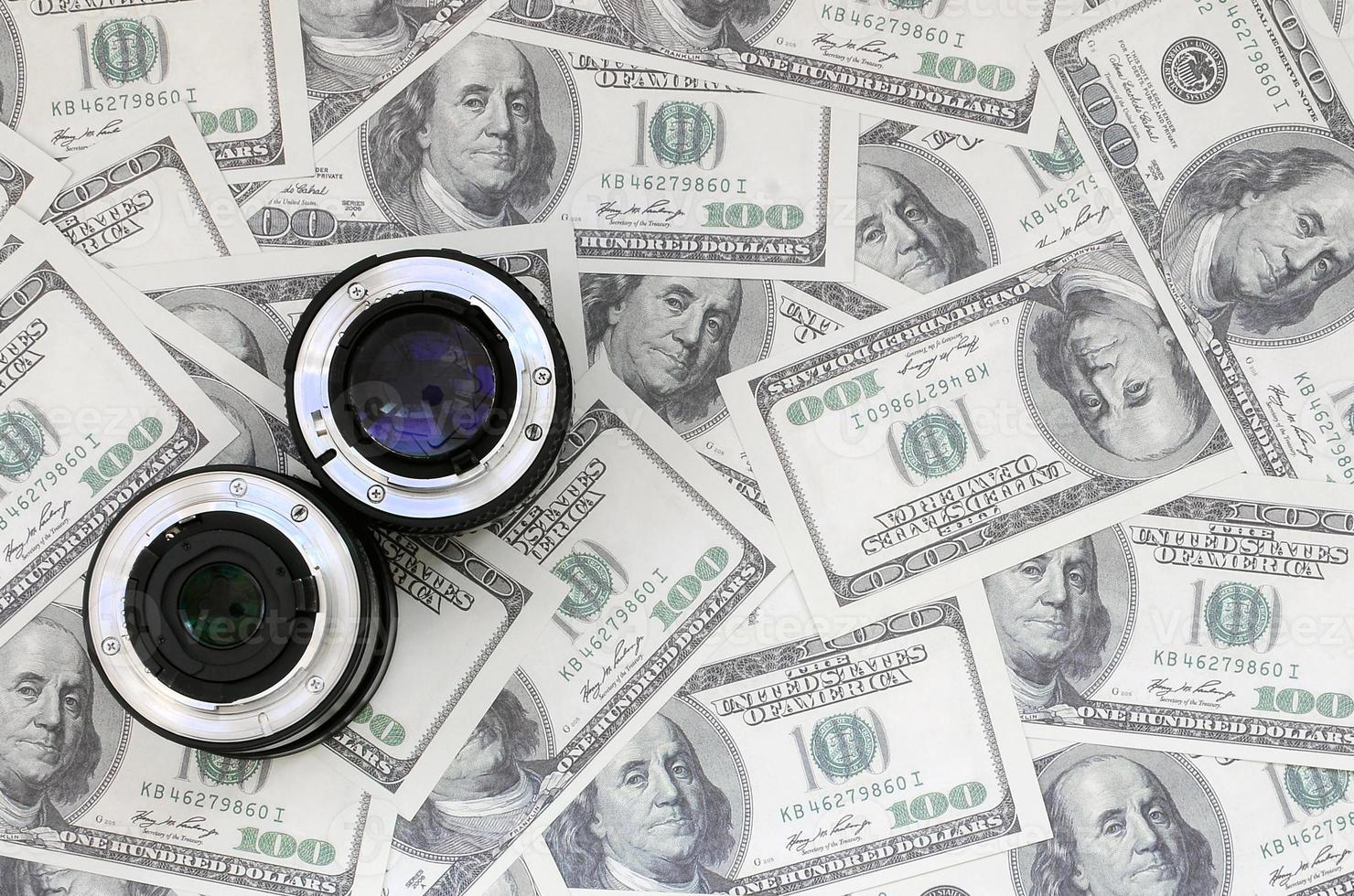 Two photographic lenses lie on the background of a lot of dollar bills. Space for text photo