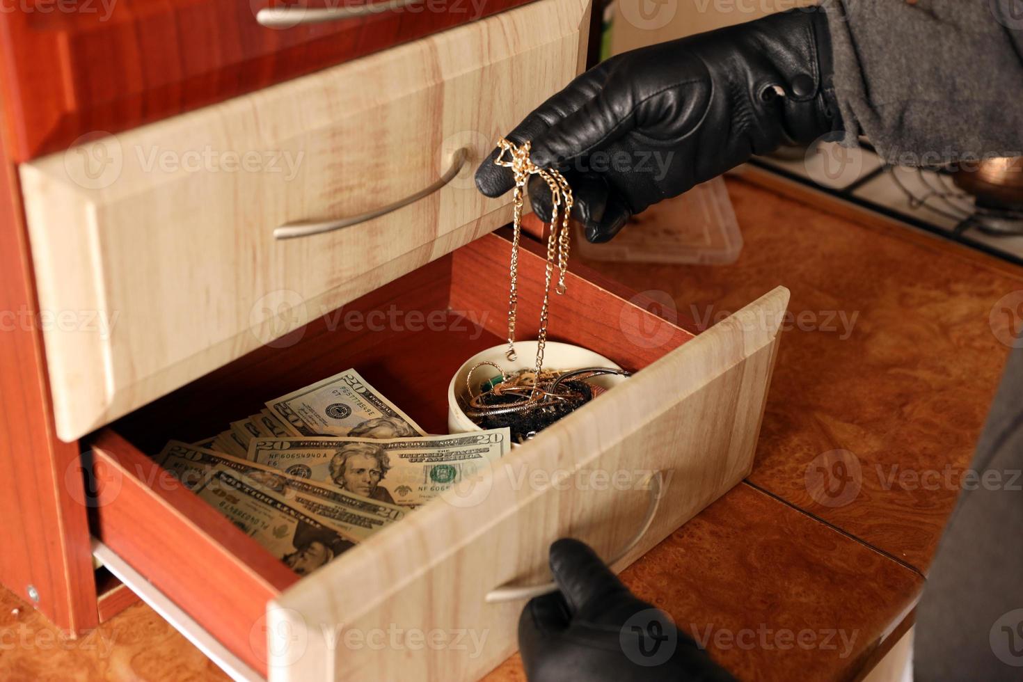 Robber in black outfit and gloves see in opened shelf in kitchen. The thief takes out the golden necklace from a shelf photo