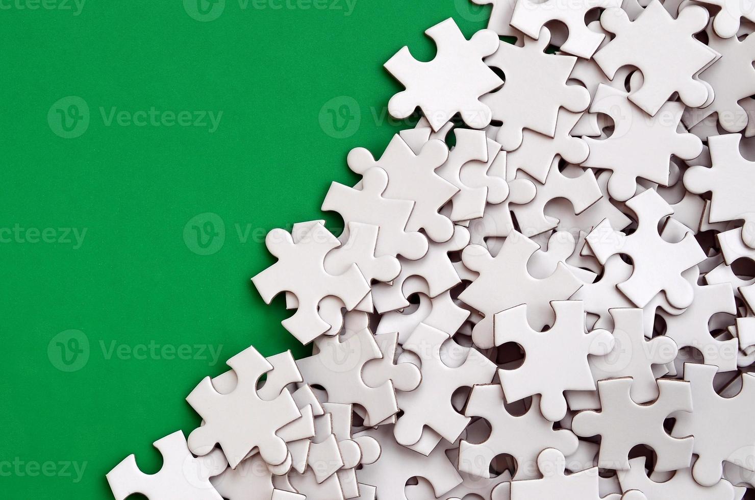 A pile of uncombed elements of a white jigsaw puzzle lies on the background of a green surface. Texture photo with copy space for text
