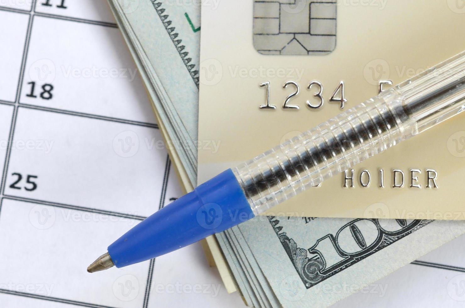 Pen and credit card on many hundred US dollar bills on calendar page close up photo