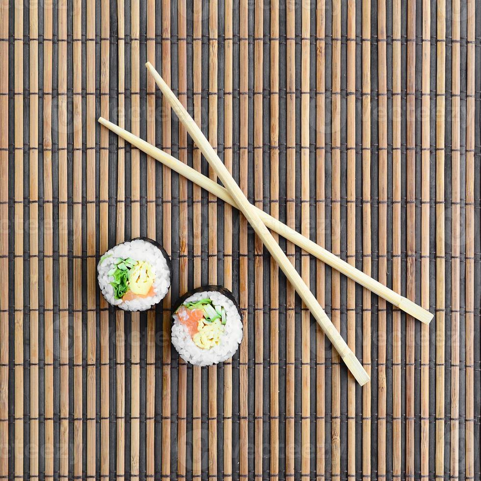 Sushi rolls and wooden chopsticks lie on a bamboo straw serwing mat. Traditional Asian food. Top view. Flat lay minimalism shot with copy space photo