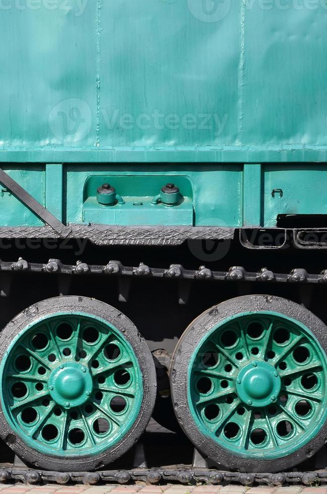 Side view of the vehicle on a caterpillar track with black tracks and green wheels and a side metal wall photo