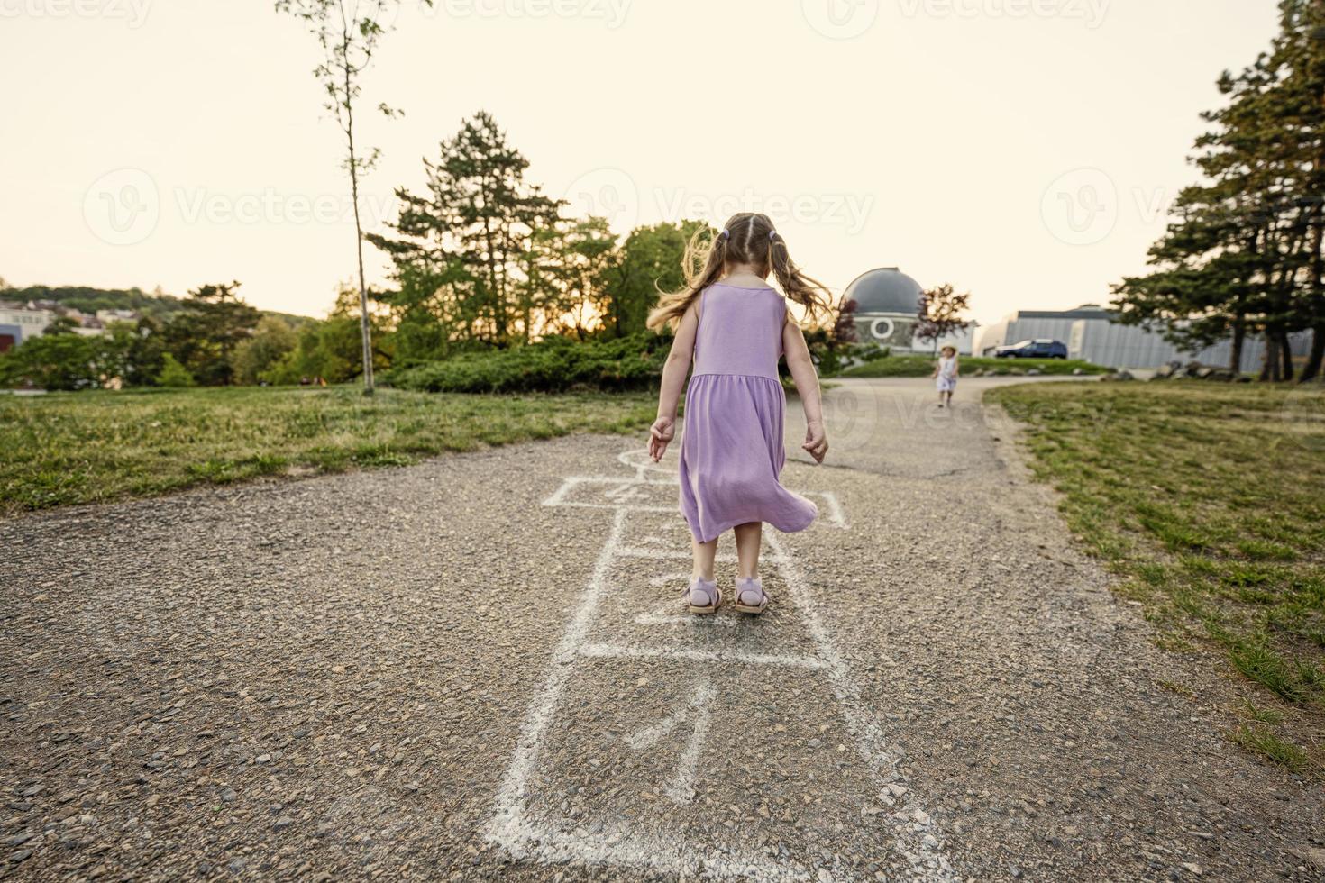 Two sisters playing hopscotch in park. Kids game, children outdoor activities. photo