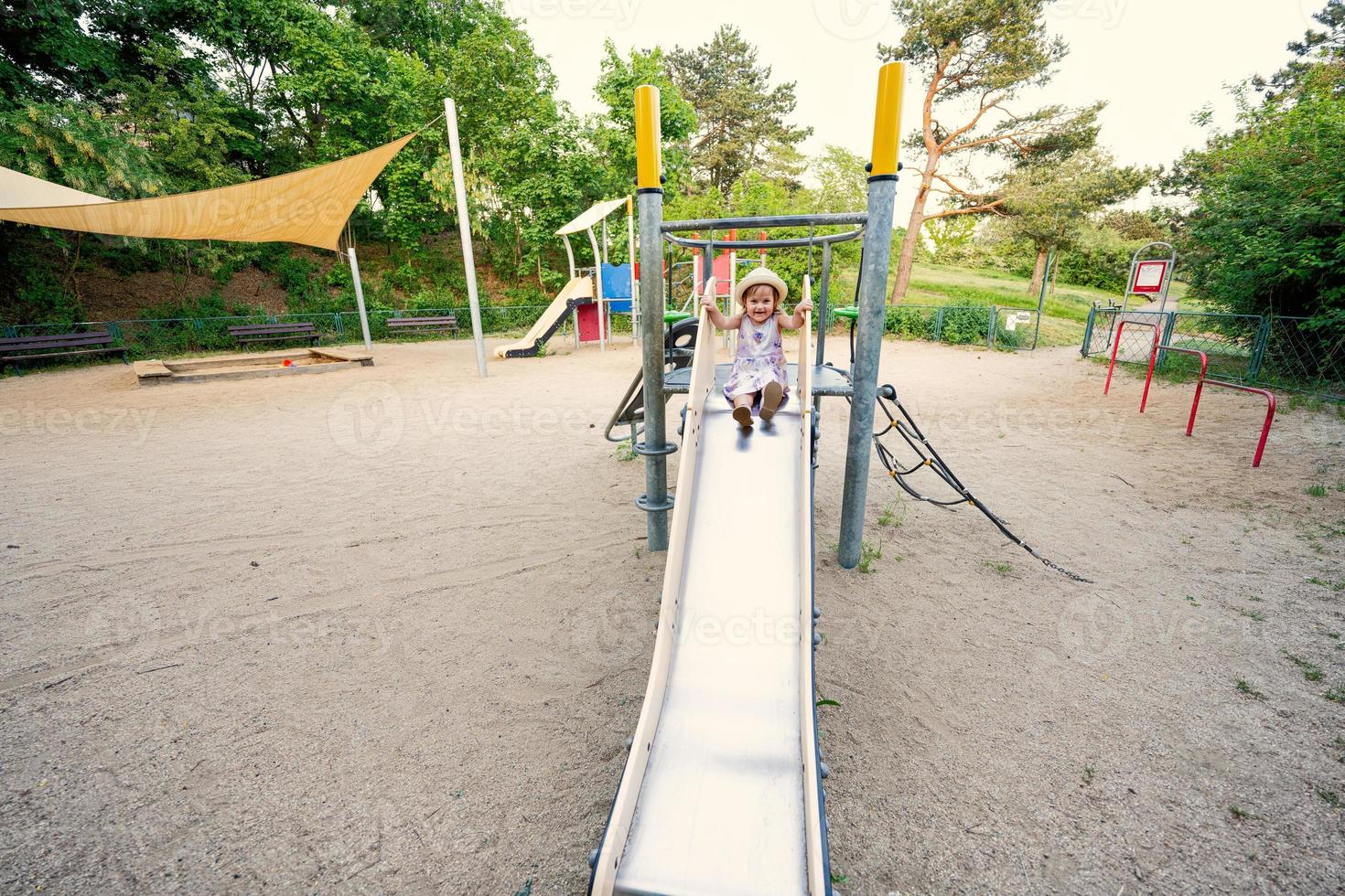 Baby girl slides in children's playground toy set in public park. photo