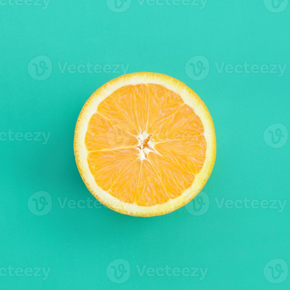 Top view of a one orange fruit slice on bright background in turquoise green color. A saturated citrus texture image photo