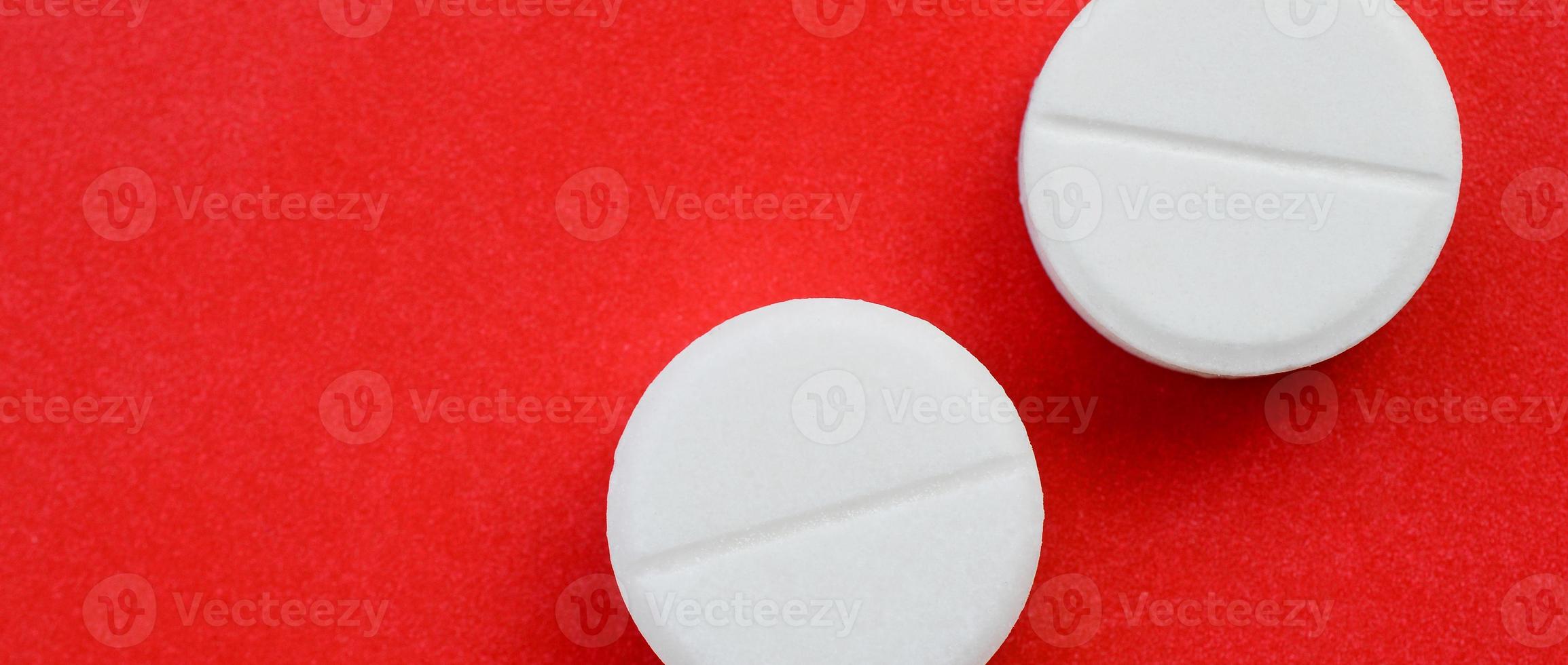 A few white tablets lie on a bright red background surface. Background image on medical and pharmaceutical topics photo