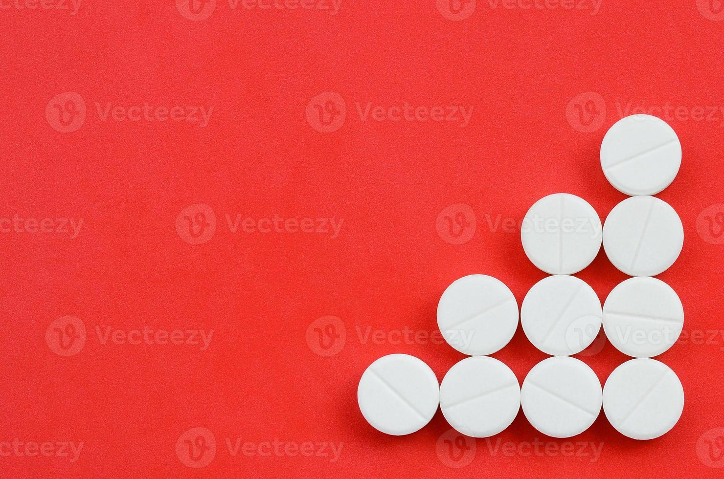 Several white tablets lie on a bright red background in the form of a triangular arrow. Background image on medicine and pharmaceutical topics photo