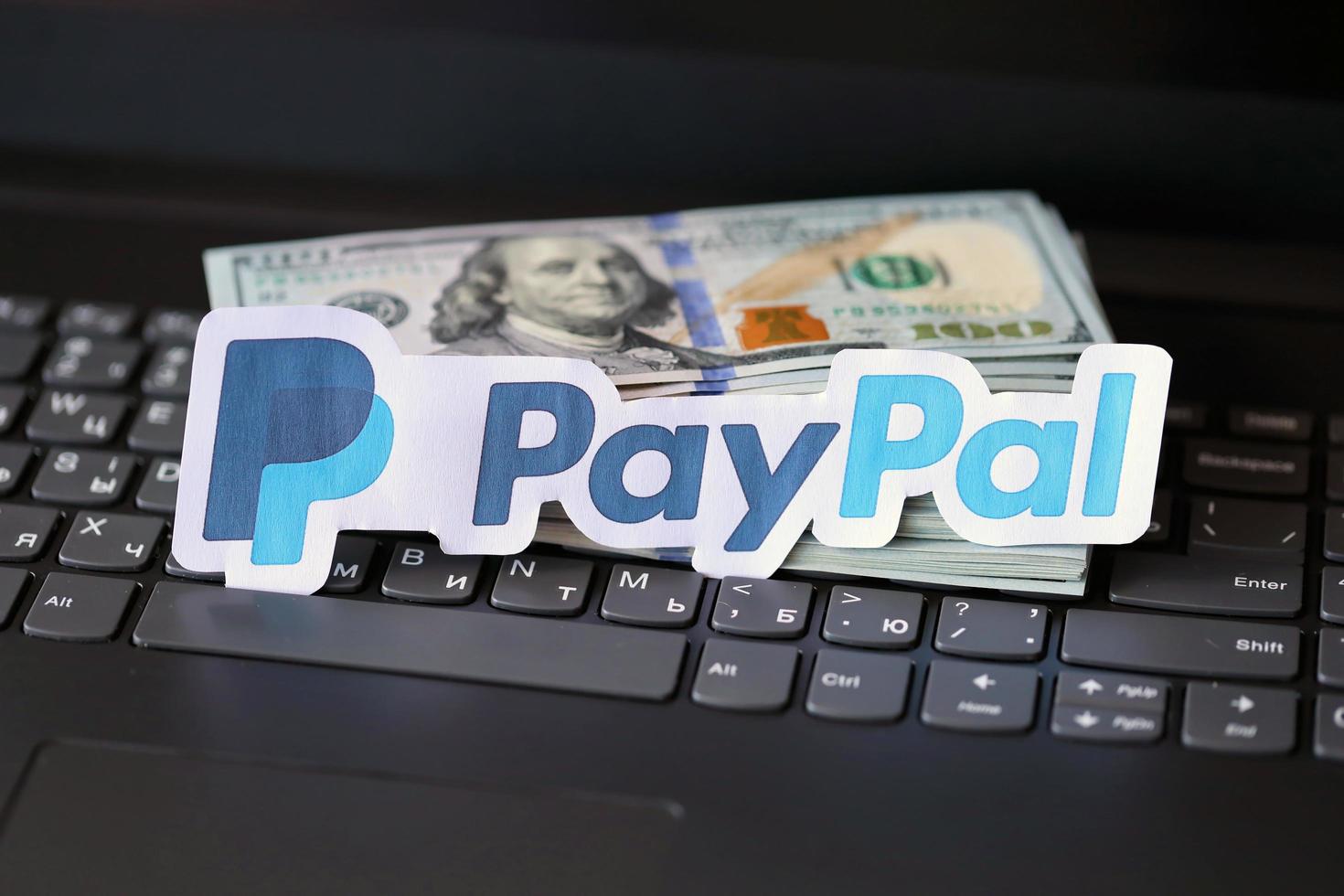 TERNOPIL, UKRAINE - SEPTEMBER 6, 2022 Payoneer paper logotype lies on black laptop with US dollar bills. Payoneer is American financial services company provides online money transfer photo