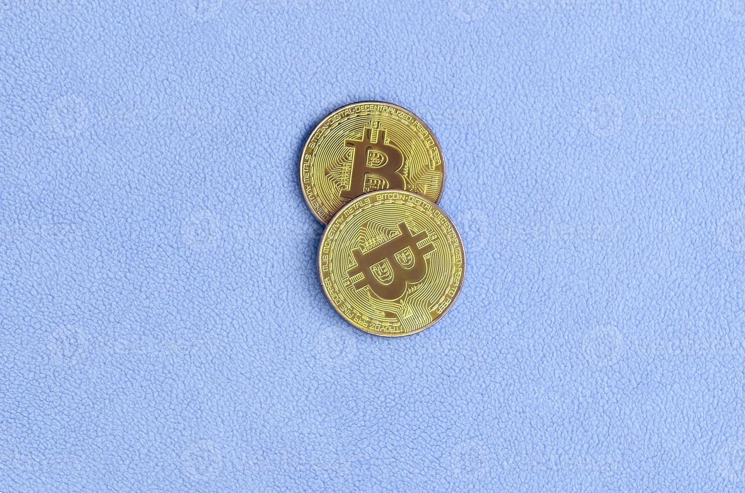 Two golden bitcoins lies on a blanket made of soft and fluffy light blue fleece fabric. Physical visualization of virtual crypto currency photo