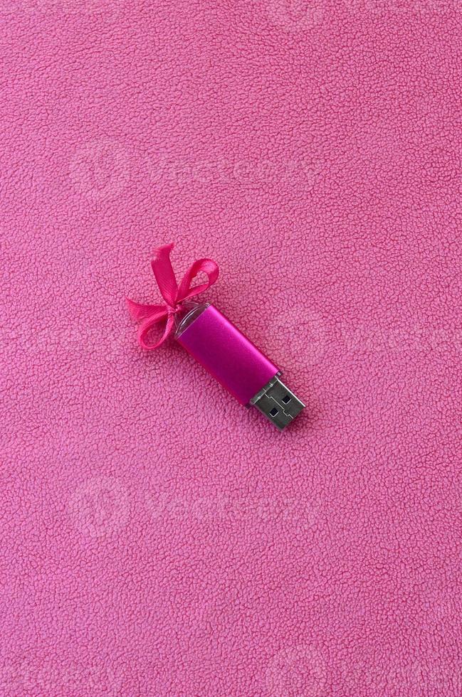 Brilliant pink usb flash memory card with a pink bow lies on a blanket of soft and furry light pink fleece fabric. Classic female gift design for a memory card photo