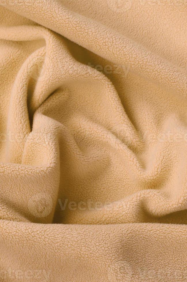 The blanket of furry orange fleece fabric. A background of light orange soft plush fleece material with a lot of relief folds photo