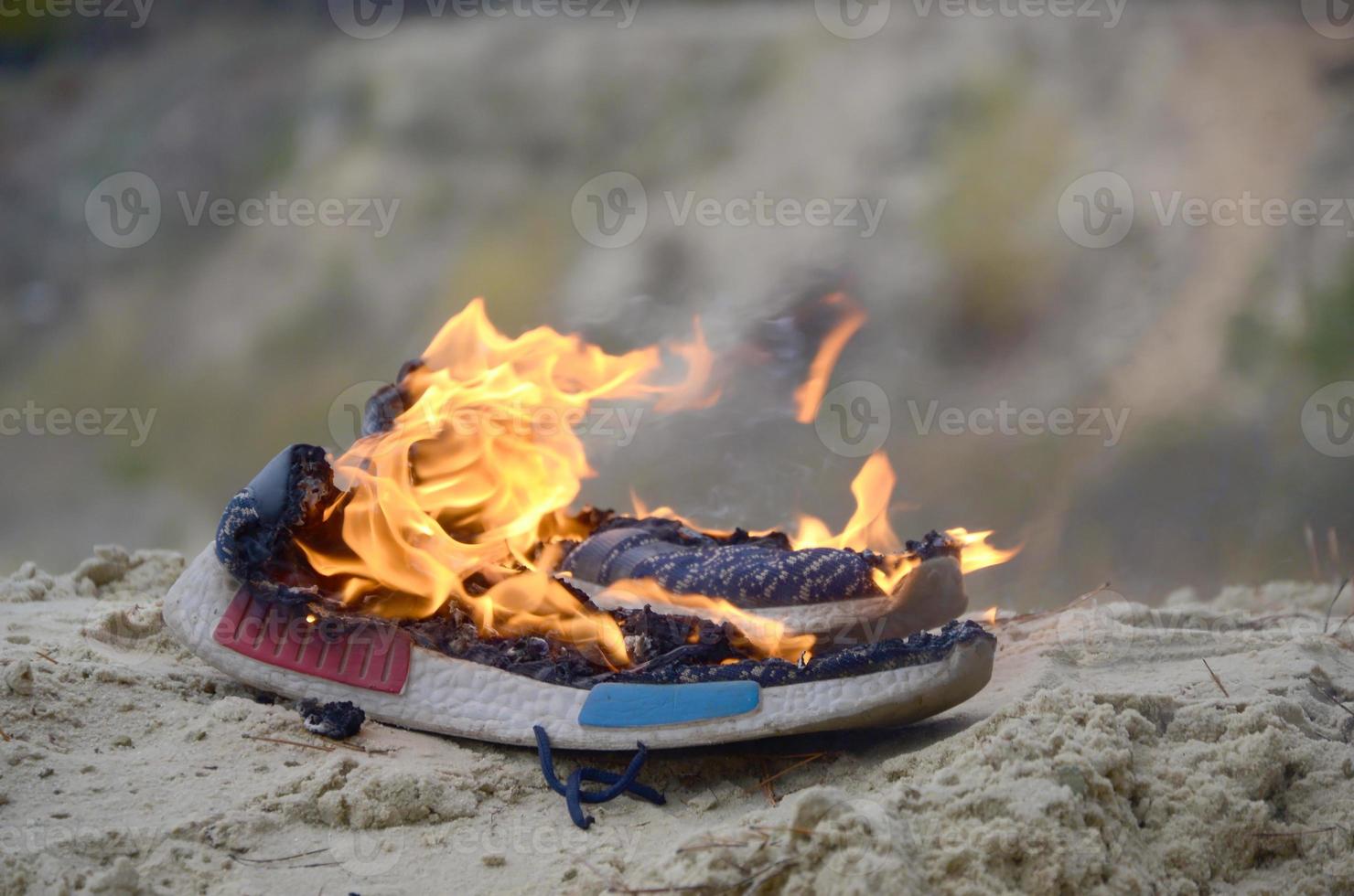 Burning sports sneakers or gym shoes on fire stand on sandy beach coast. Athlete burned out. Physical exertion during training concept photo