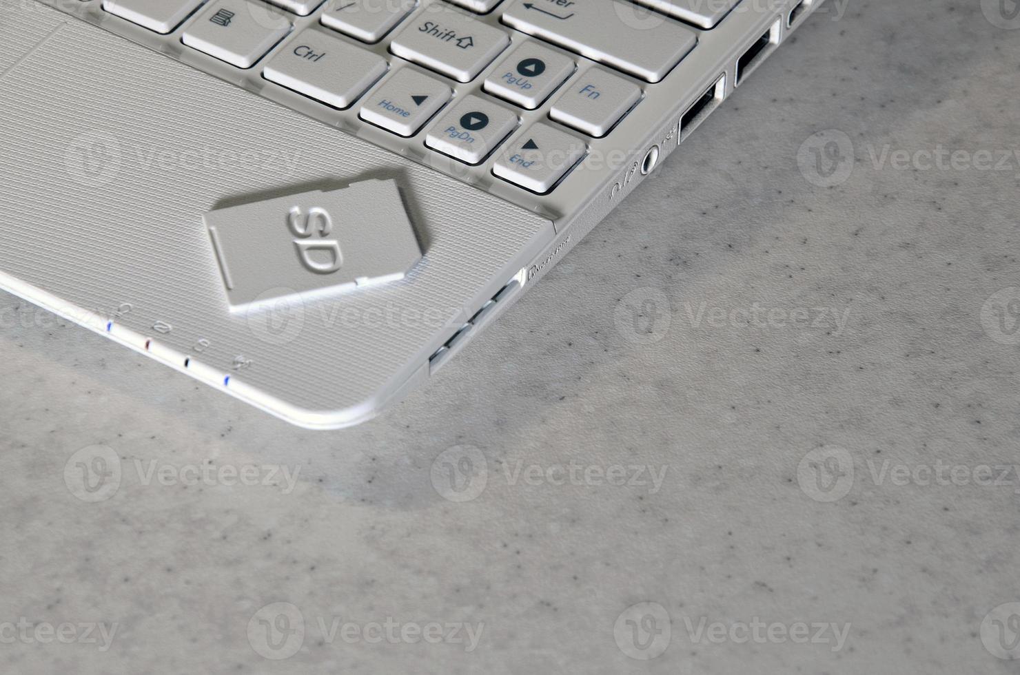 A compact SD memory card lies on a white netbook. The digital information storage device is ready for use. Concept of modern technologies photo