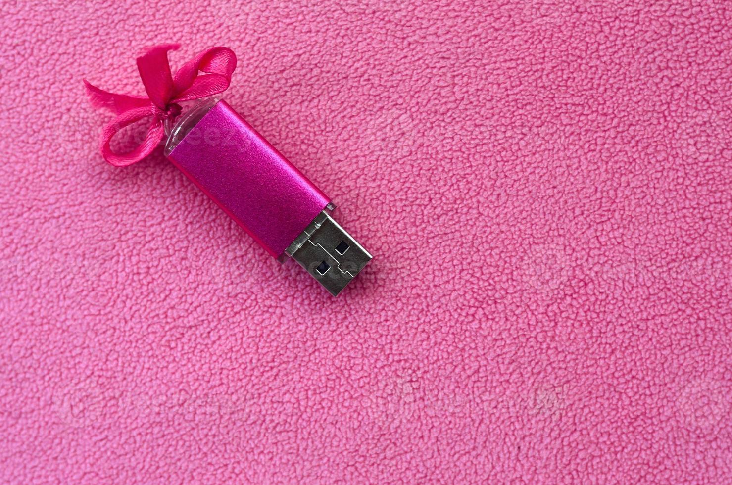 Brilliant pink usb flash memory card with a pink bow lies on a blanket of soft and furry light pink fleece fabric. Classic female gift design for a memory card photo