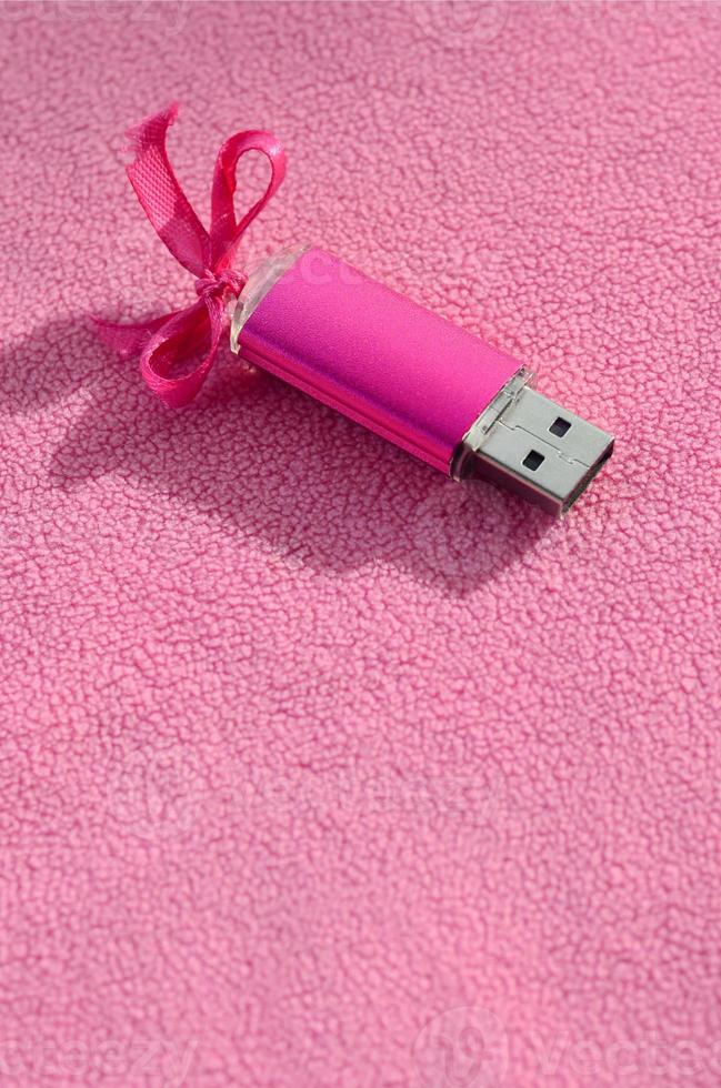 Brilliant pink usb flash memory card with a pink bow lies on a blanket of soft and furry light pink fleece fabric. Classic female gift design for a memory card photo