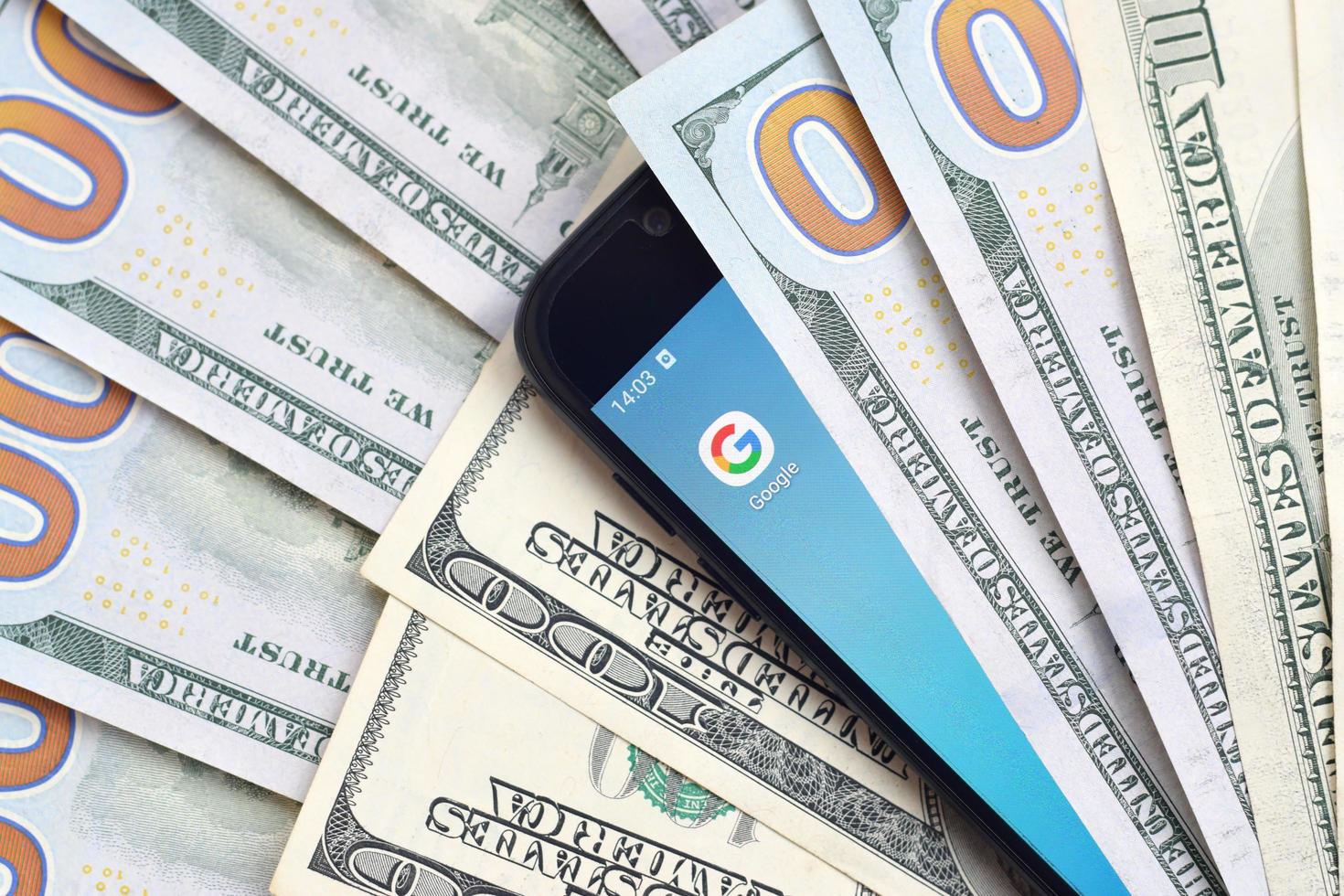 KHARKOV, UKRAINE - JULY 2, 2021 Smartphone screen with Google app and lot of hundred dollar bills. Business and social networking concept photo