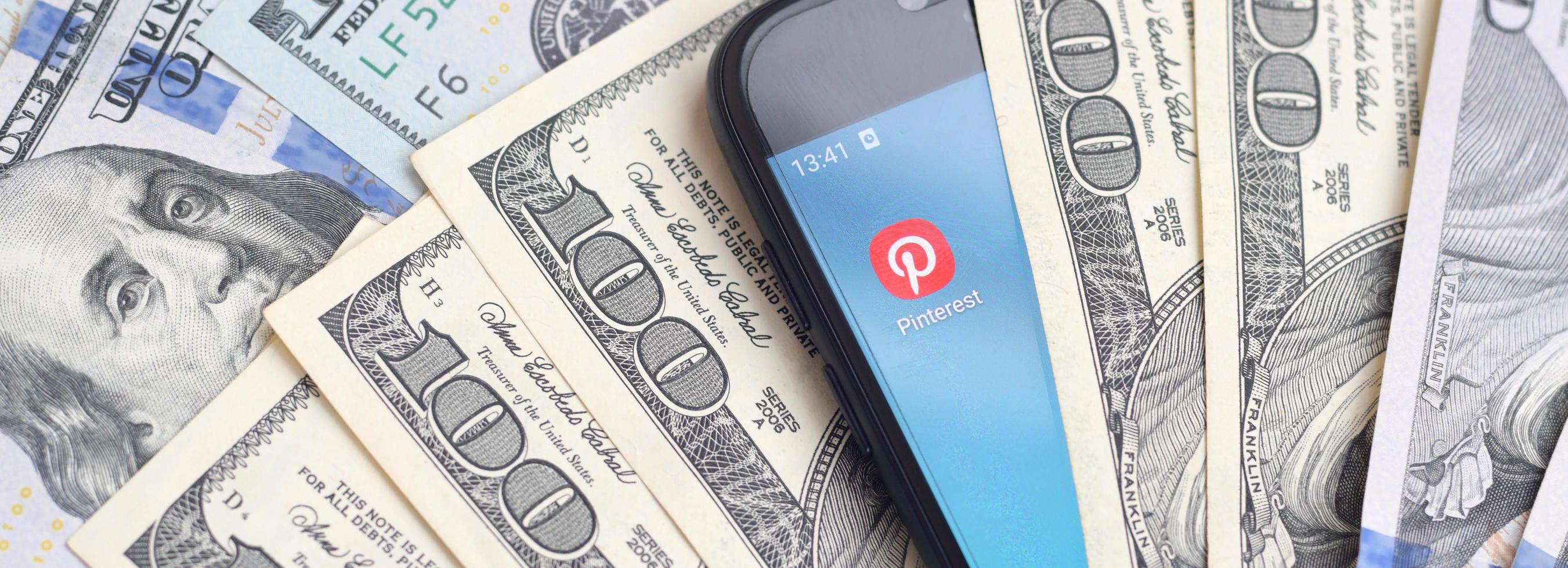 KHARKOV, UKRAINE - JULY 2, 2021 Smartphone screen with Pinterest app and lot of hundred dollar bills. Business and social networking concept photo