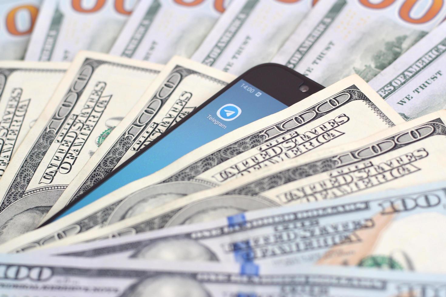 KHARKOV, UKRAINE - JULY 2, 2021 Smartphone screen with Telegram app and lot of hundred dollar bills. Business and social networking concept photo