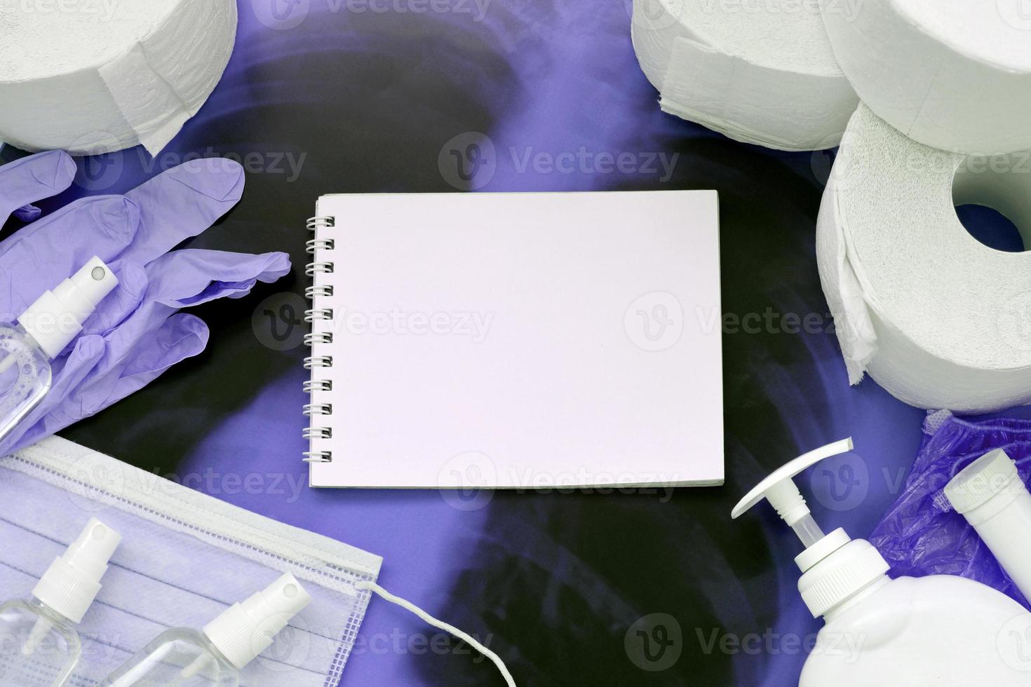 Set of items for Covid-19 quarantine. Empty notepad page and toilet paper, rubber gloves with surgical face mask and hand sanitizer with liquid soap bottle on human chest x-ray film photo