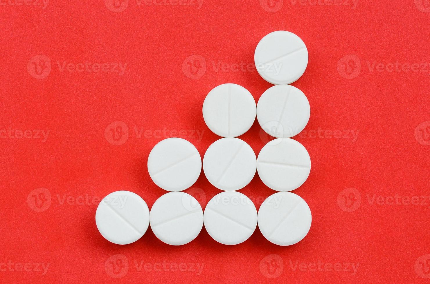 Several white tablets lie on a bright red background in the form of a triangular arrow. Background image on medicine and pharmaceutical topics photo