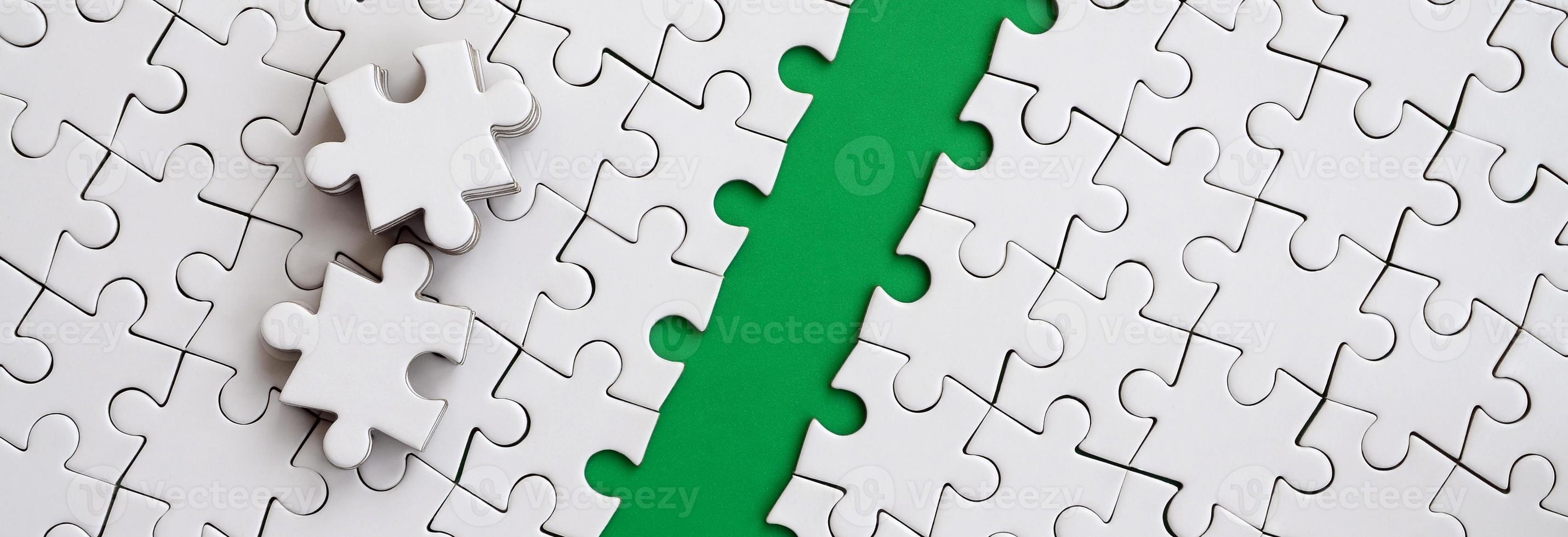 The green path is laid on the platform of a white folded jigsaw puzzle. The missing elements of the puzzle are stacked nearby. Texture image with space for text photo