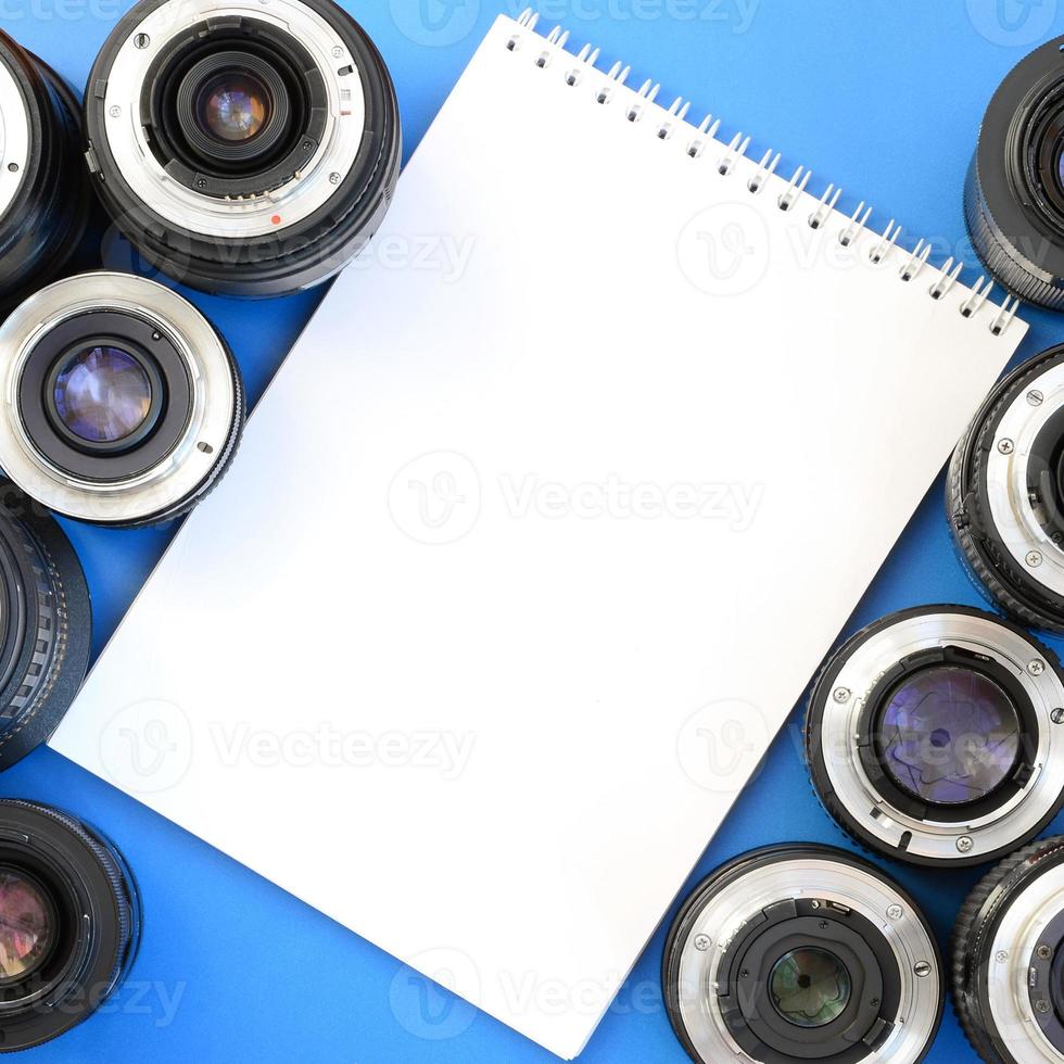 Several photographic lenses and white notebook lie on a bright blue background. Space for text photo