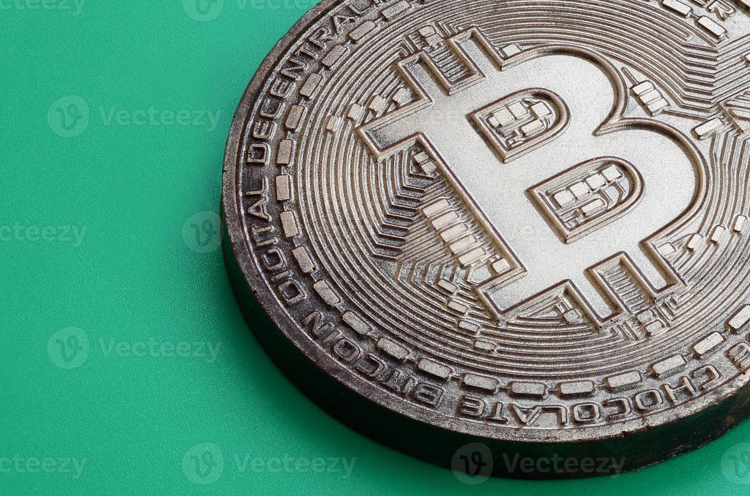 Chocolate product in the form of physical bitcoin lies on a green plastic background. Model of the crypto currency in the edible form photo